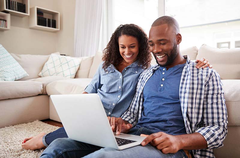 Young,Black,Couple,Using,Laptop,Sitting,On,The,Floor,At