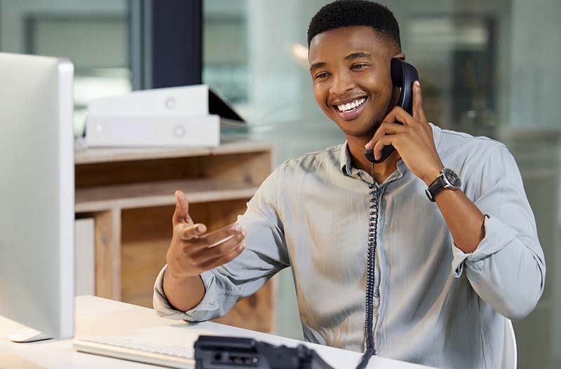 Shot of a young man using a telephone and computer in a modern office